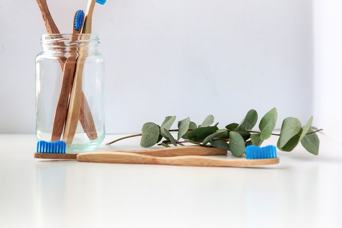 Wooden-handled toothbrushes in a glass jar beside eucalyptus leaves